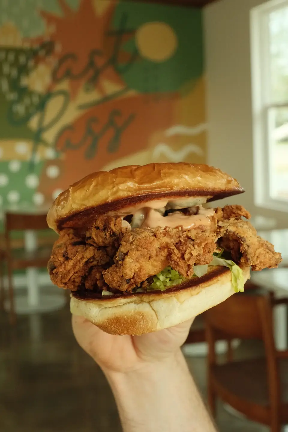 Crispy chicken sandwich held up in front of the mural