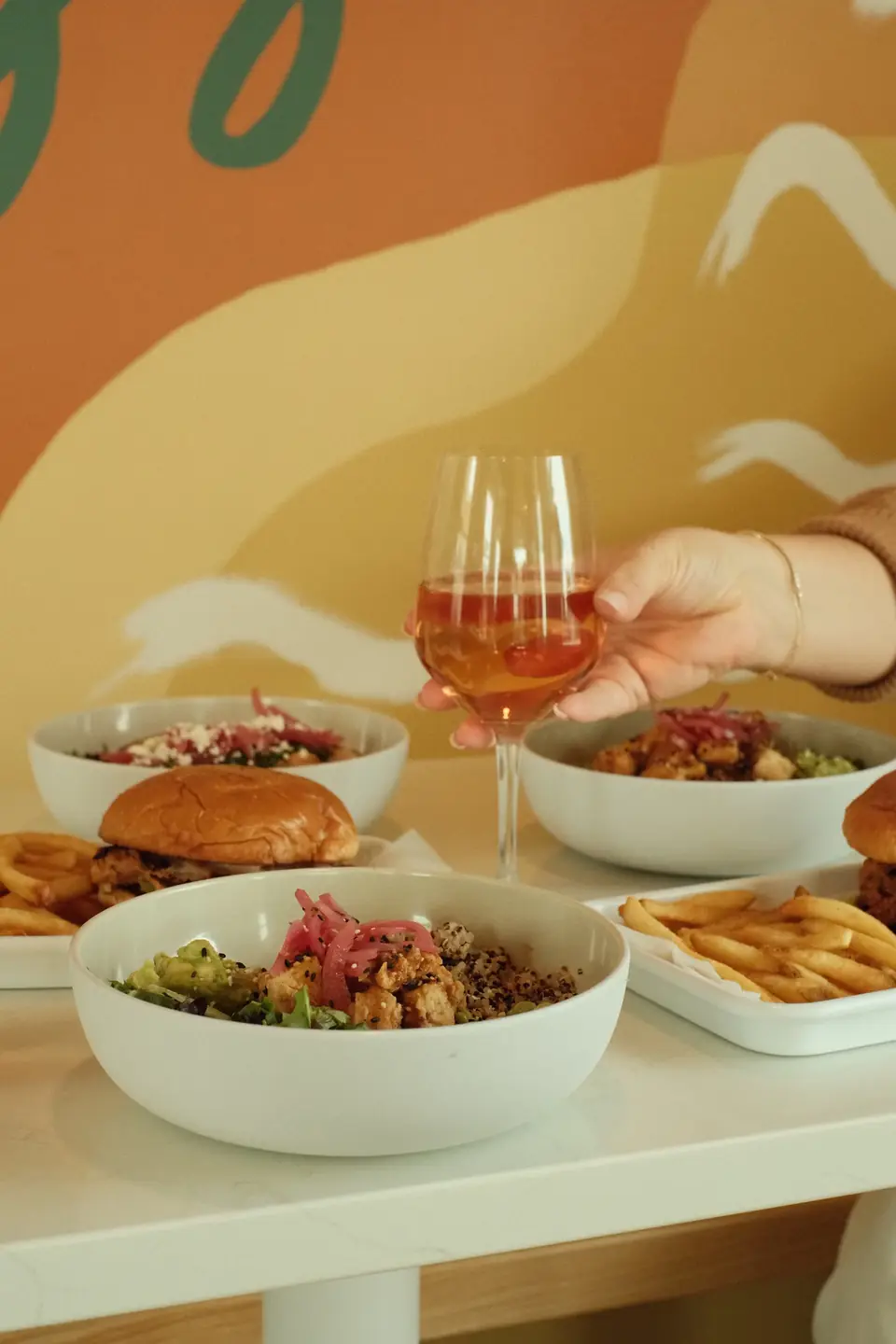 A glass of rosé and a spread of food at the mural