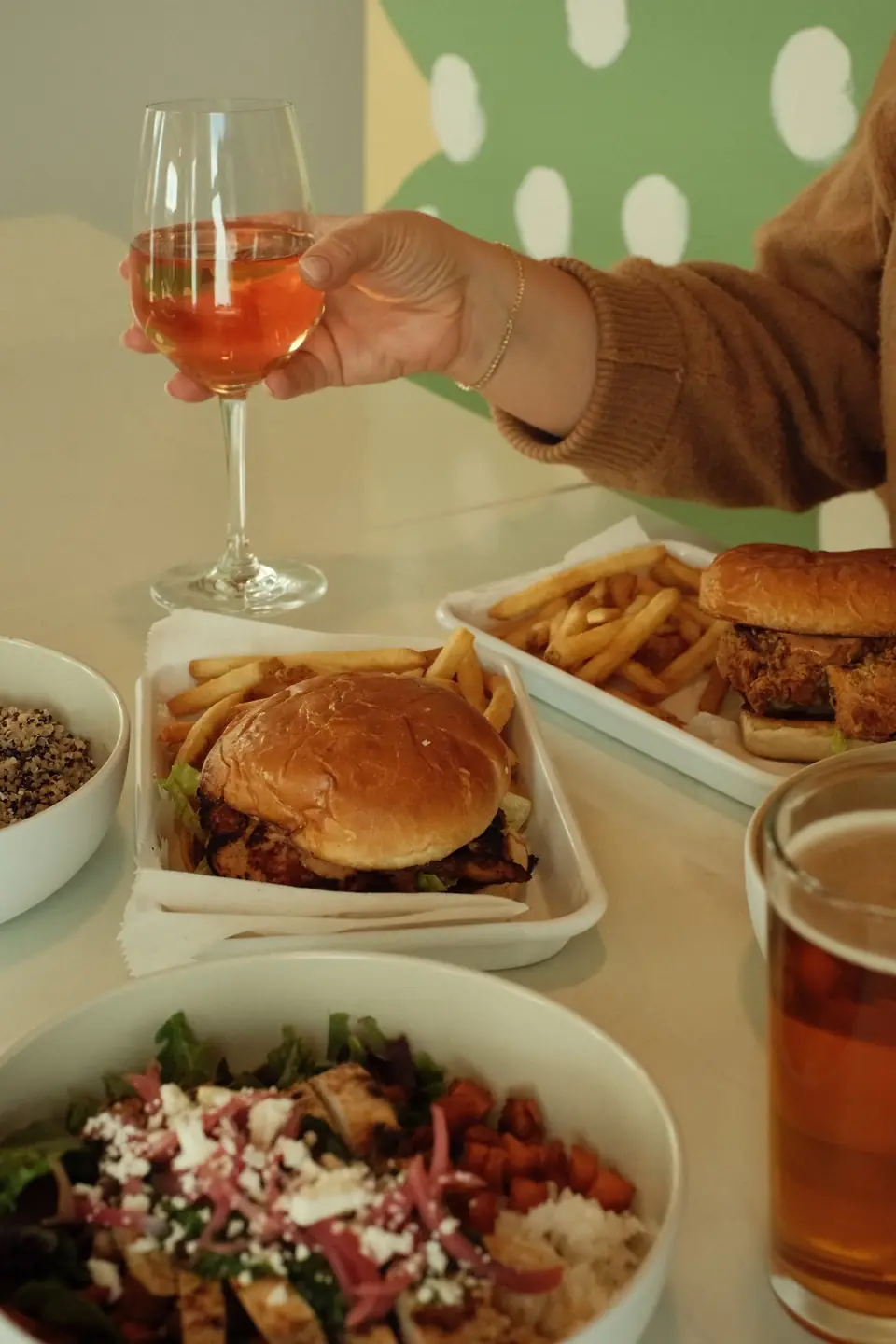 A glass of rosé raised over burgers, fries and bowls